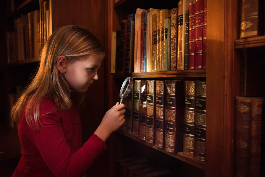 En flicka tittar på böcker i en bokhylla med ett förstoringsglas.