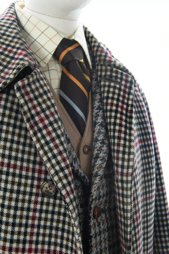 En rutig herrutstyrsel med överrock, blazer, skjorta väst och randig slips på en docka.