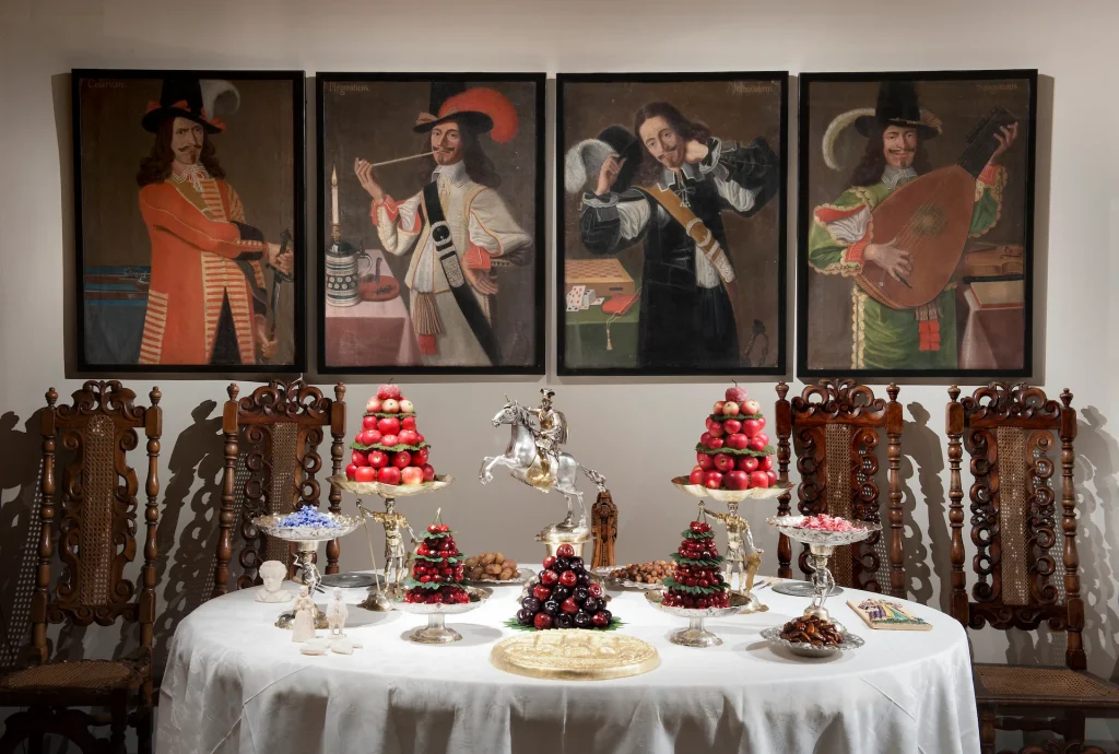 Ett festbord står dukat med festliga efterrätter, bakom syns tavlor från 1600-talet.