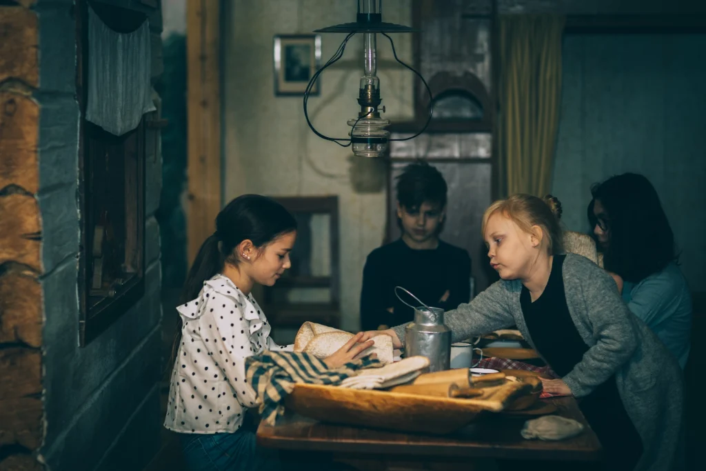 Tre barn sitter runt matbordet i ett bondkök.