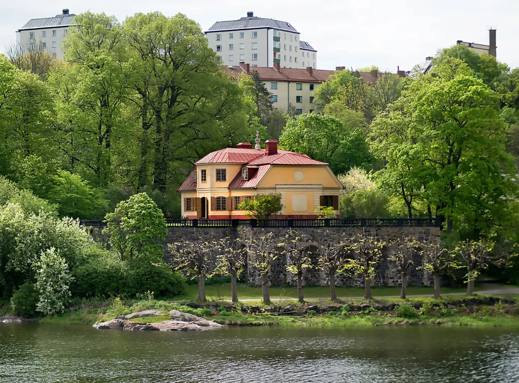 Gul liten herrgård vid vatten, i bakgrunden syns höghus.