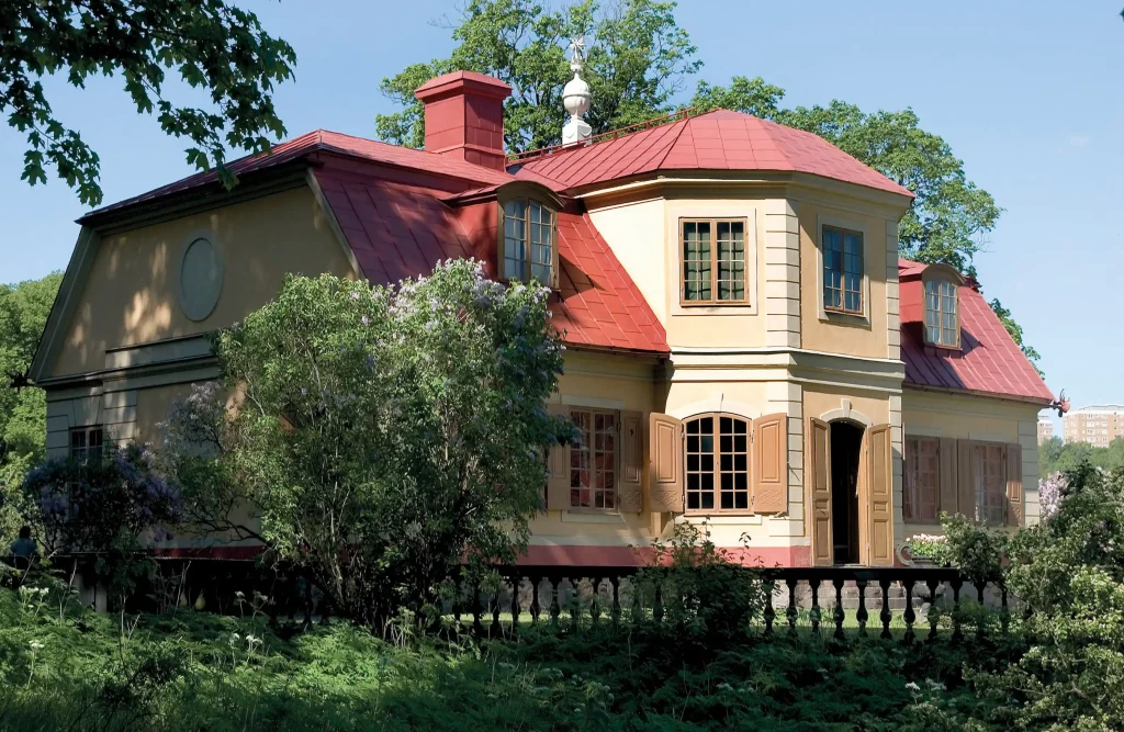 A yellow manor house surrounded by a lush garden.