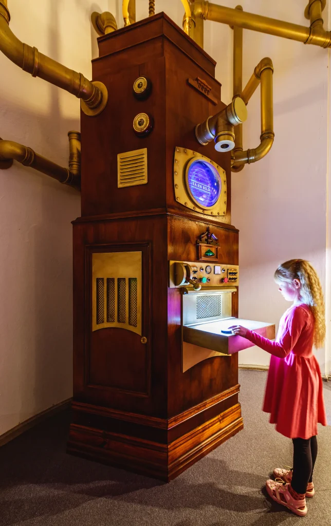 En märklig stor maskin med rör och knappar och en digitalskärm, en flicka skickar in ett papper i maskinen.