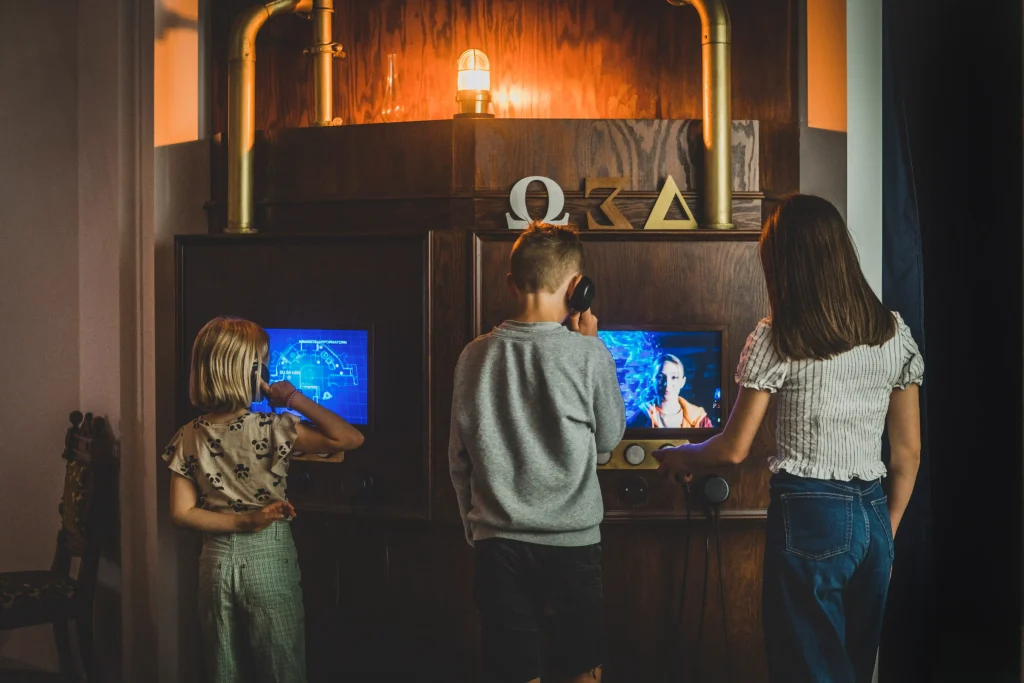 Två flickor och en pojke står och lyssnar och jobbar vid digitala skärmar.