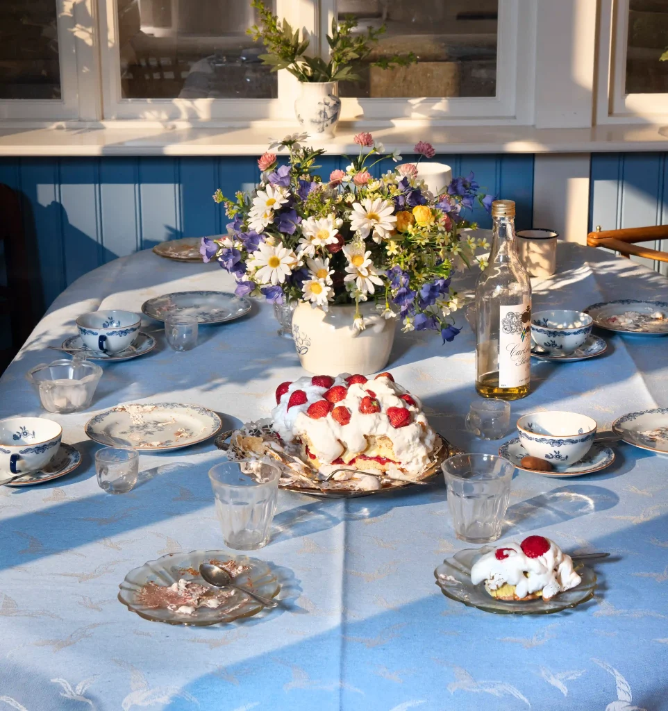 Vas med sommarblommor på dukat bord för fika med jordgubbstårta.