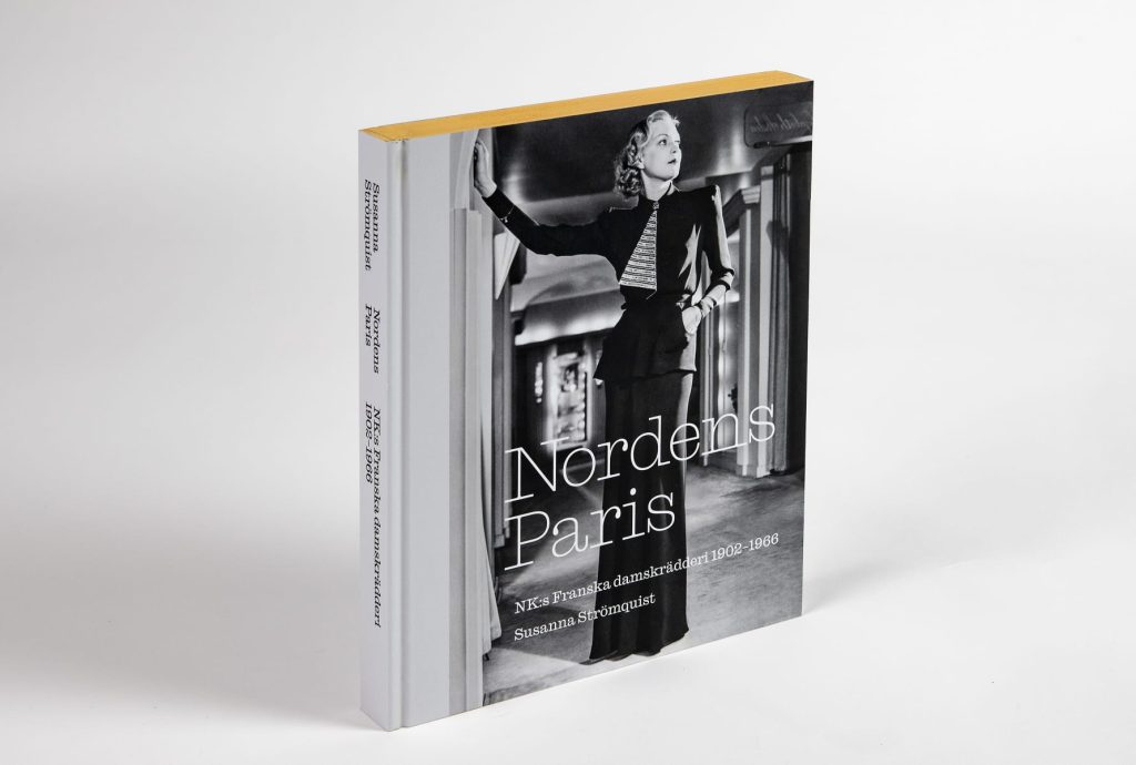 En bok med guldsidor och en modebild på en kvinna i svart knytblus och vid långbyxa.