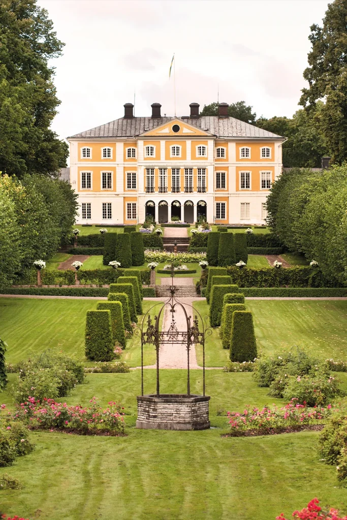 En gul herrgård med formklippta häckar och park framför.