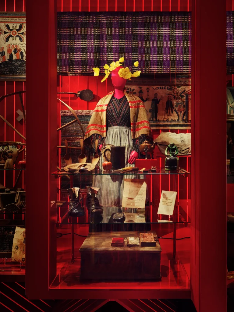 Utställningsmonter i starka röda färger. I montern syns bland annat en klädd docka.