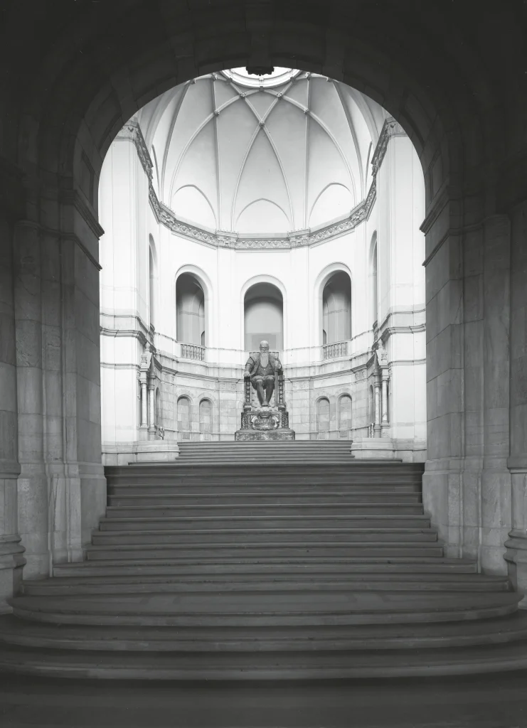 A staircase leads up to a large hall with skylights, arches, and pillars, featuring a large statue of an elderly Gustav Vasa in plaster.