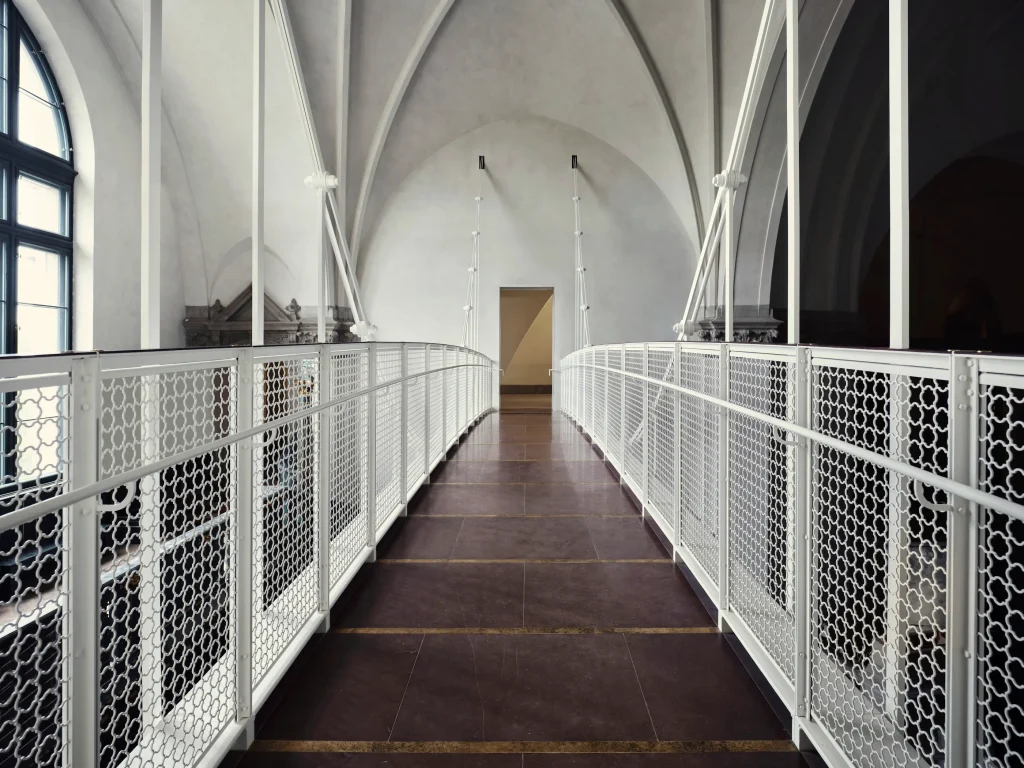 A sightline from one side of a bridge to the other, featuring white railings and a burgundy stone floor.