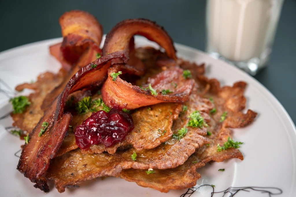 En närbild av en tallrik med raggmunk, bacon och lingonsylt.
