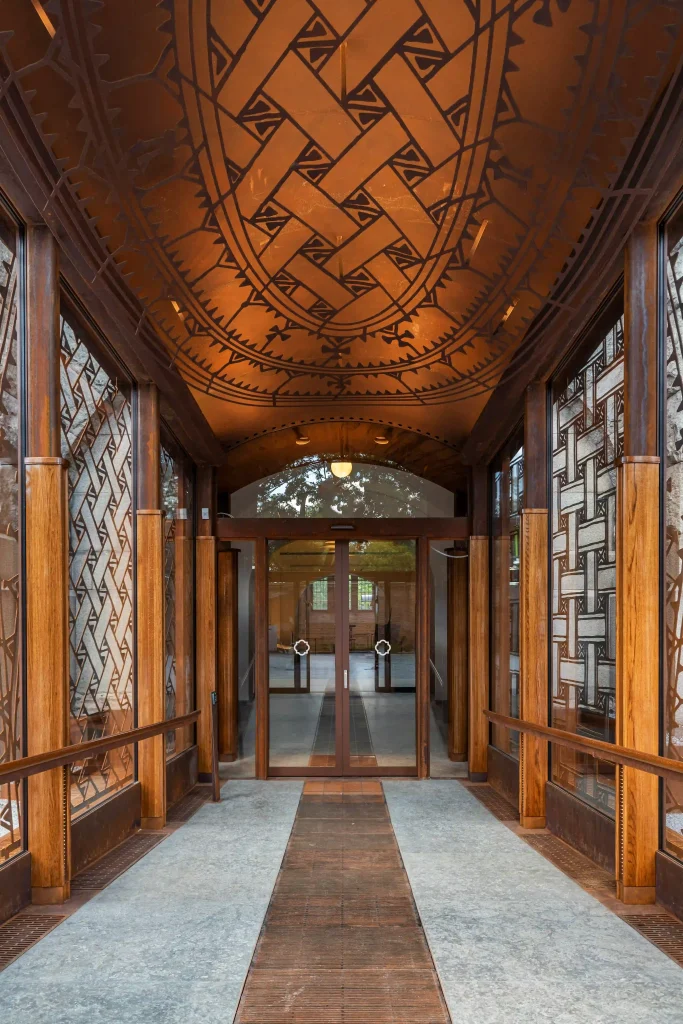 Man ser in mot två glasdörrar genom en glasad gång, taket och väggarna har ett flätat mönster.
