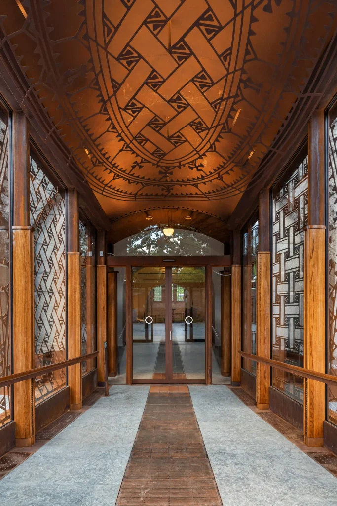 One sees through a glass corridor towards two glass doors; the ceiling and walls have a woven pattern.