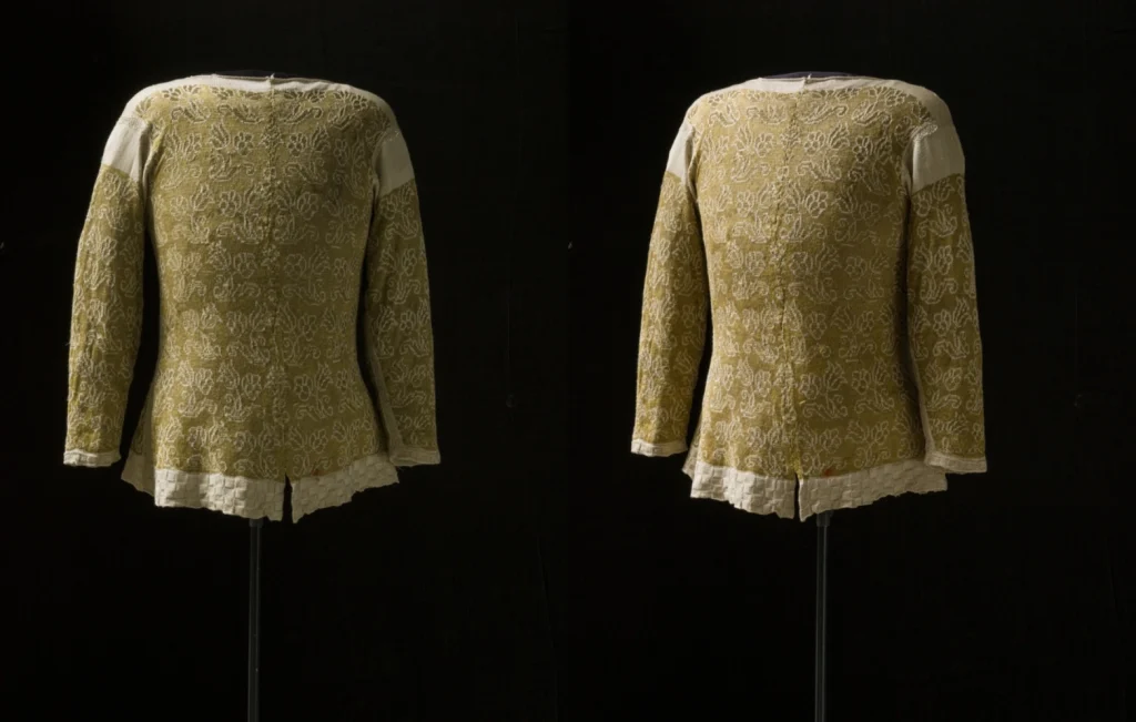 Två tröjor av gult silke från 1600-talet monterade på skyltdockor mot en svart bakgrund. Båda har vita detaljer på axlar och i kanter och ett mönster i form av vita tulpaner.