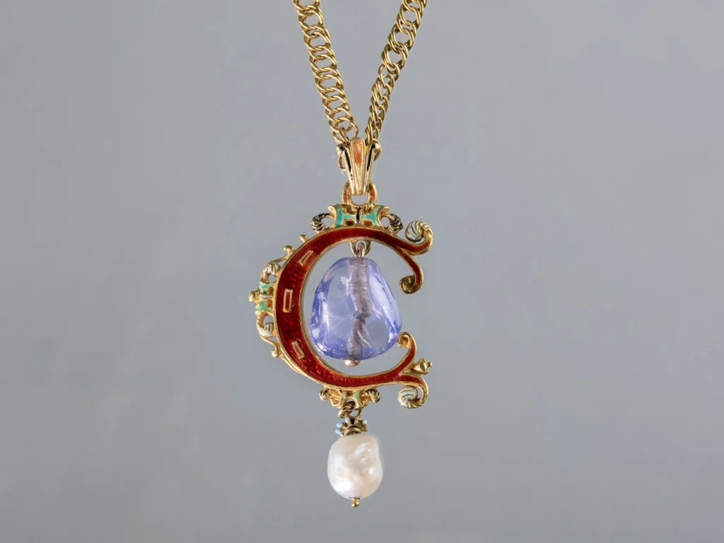 Ett halssmycke i en guldkedja, smycket är format som bokstaven C och har en safir och en pärla.