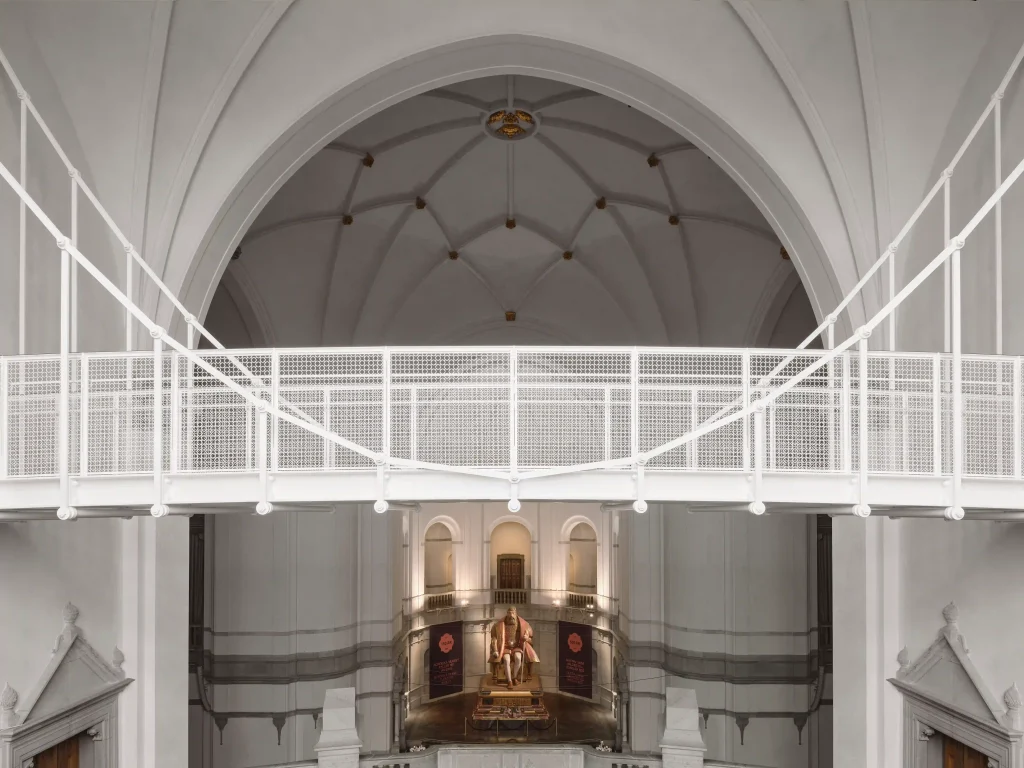 En vit hängbro i en sal med höga kryssvalv i taket och en staty av Gustav Vasa.