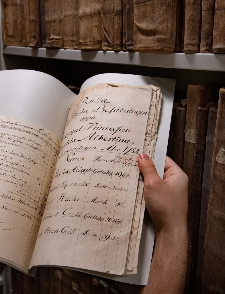 En hand håller i en arkivmapp med anteckningar i snirklig gammaldags handstil som ser ut att vara skriven med skrivstift.
