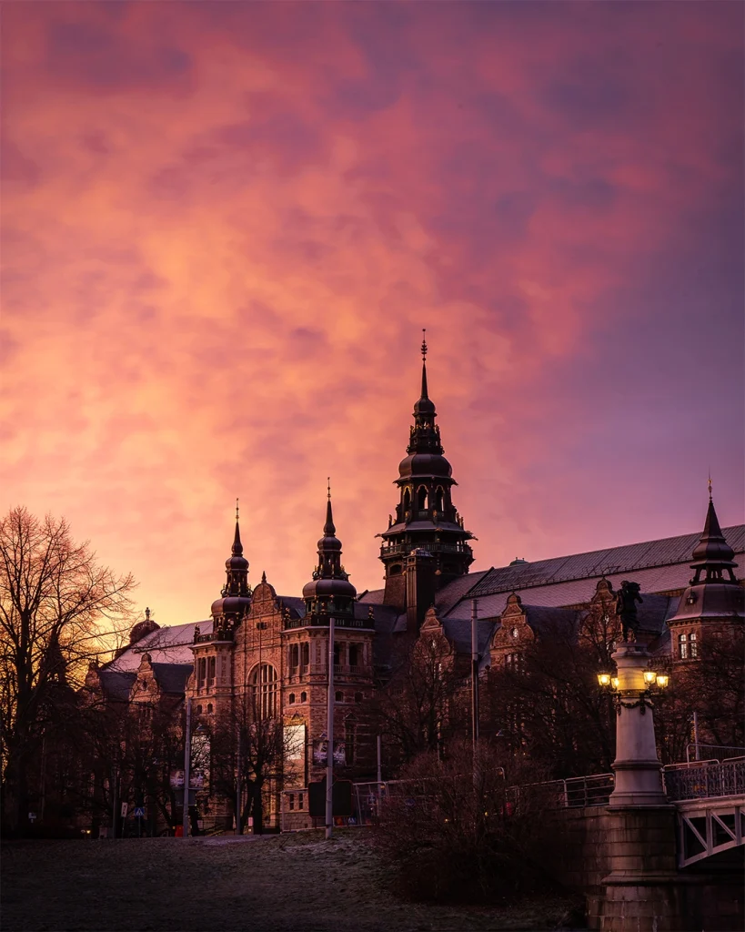 Nordiska museet i vårskymning mot en dramatisk himmel i gult, rosa och lila.