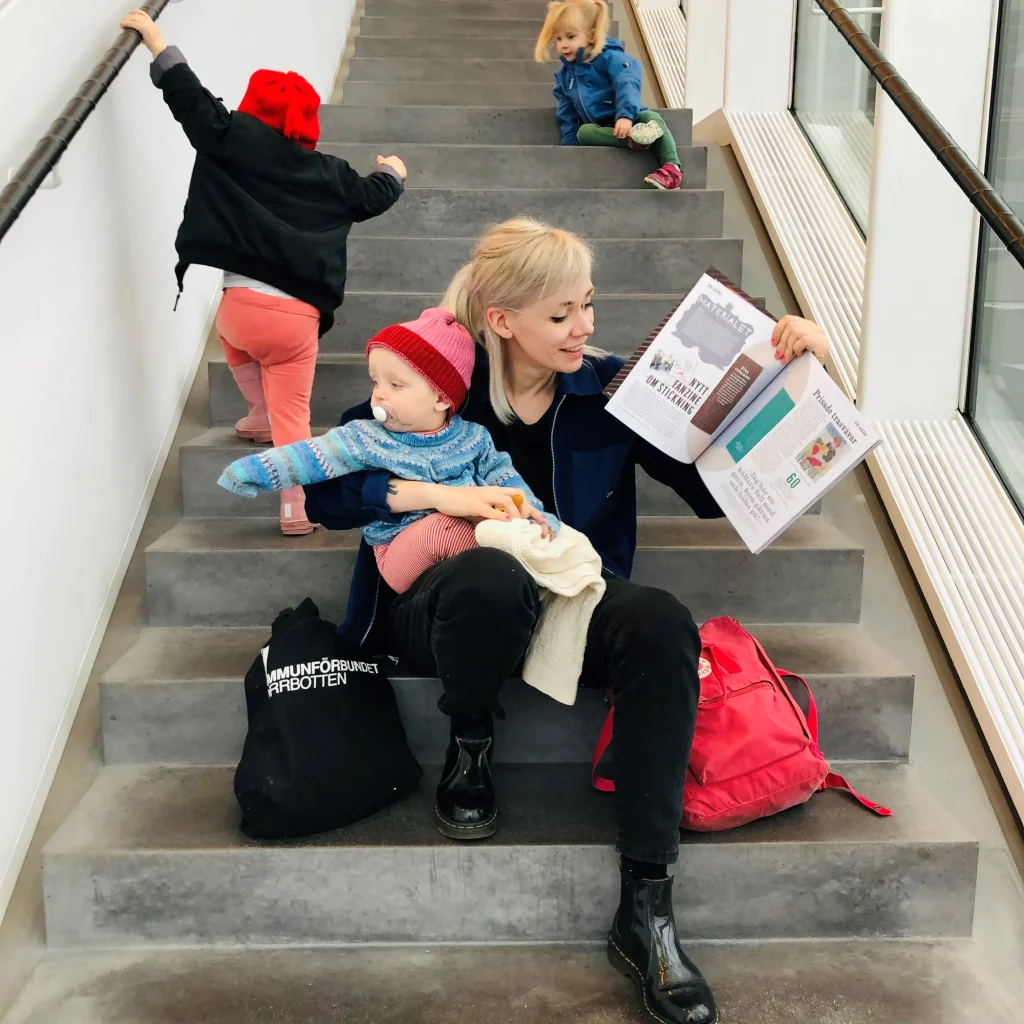 Kvinna sitter med barn och fanzine i en trappa.