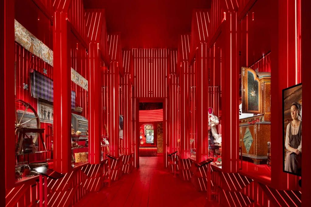 En gång genom ett starkt rött rum med montrar med föremål och skärmar med filmscener om två av utställningens personöden.