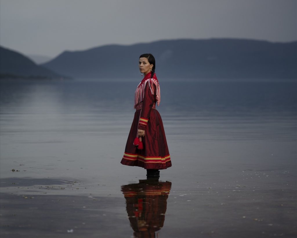 En kvinna i samiska kläder står i en sjö.