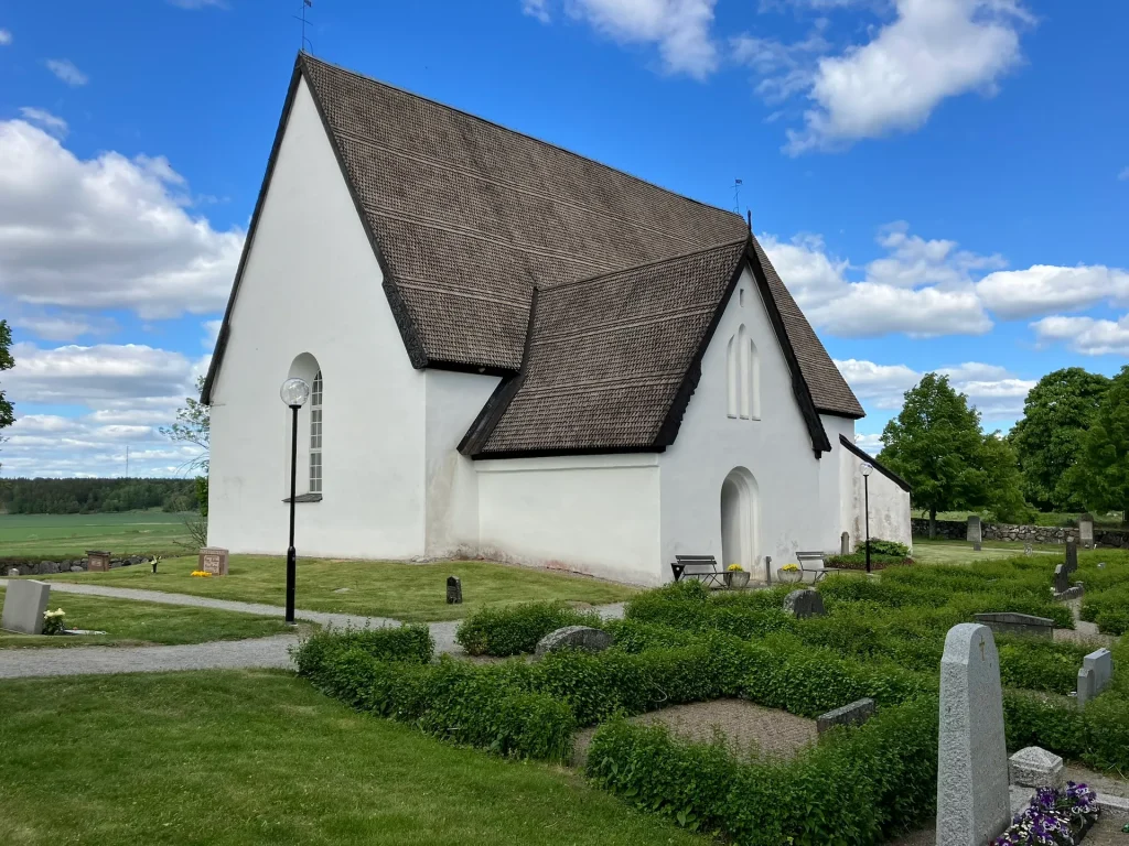 En vitkalkad medeltida kyrka med trätak i lantlig miljö.