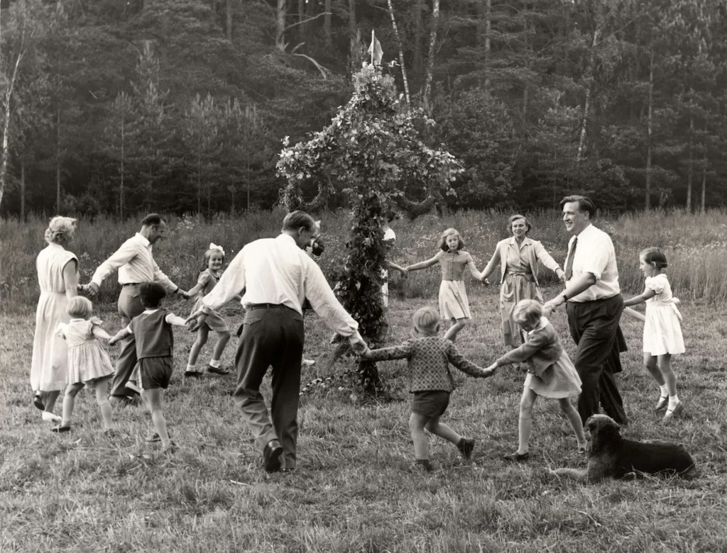 Vuxna och barn som dansar runt en midsommarstång.
