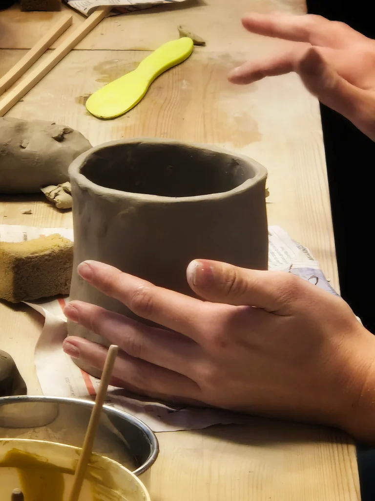 En hand formar lera till en vas eller mugg