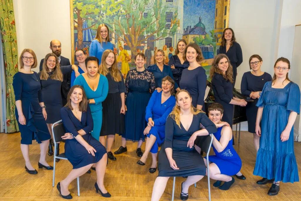 Stockholms akademiska damkör står uppställda i ett rum. Alla har blå kläningar.