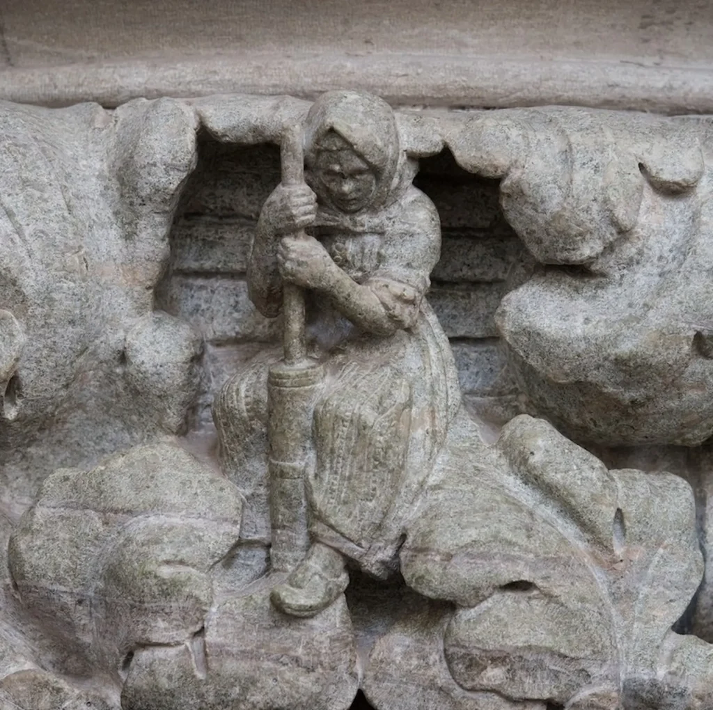 Närbild av kapitälskulptur, en kvinna i huckle som kärnar smör.