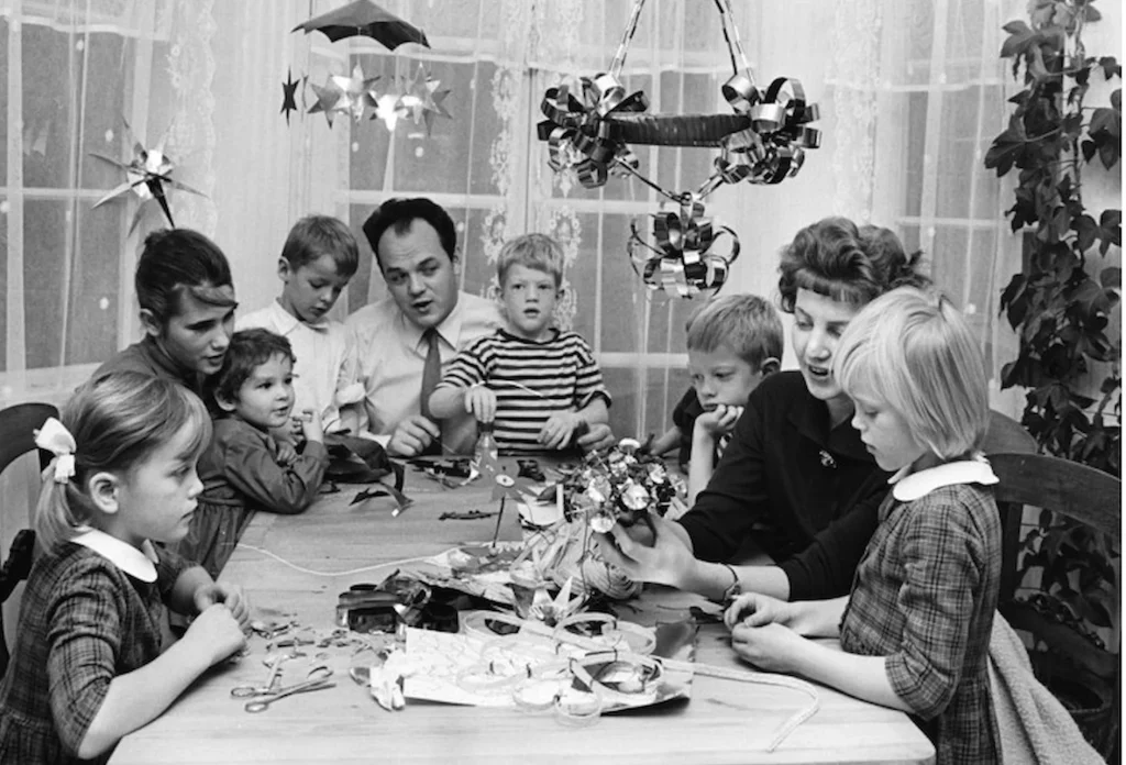 Svartvitt fotografi av vuxna och barn som sitter vid ett bor och julpysslar