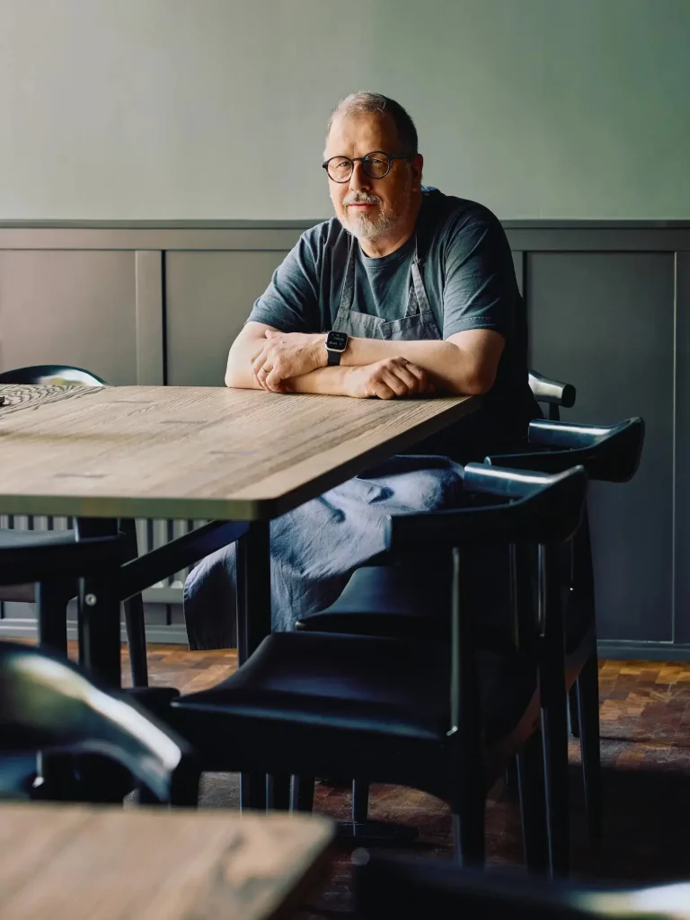 En man sitter i förkläde vid ett matbord.