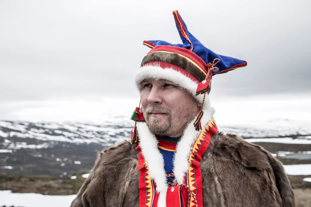 En samisk man i samisk dräkt blickar ut över fjällen.