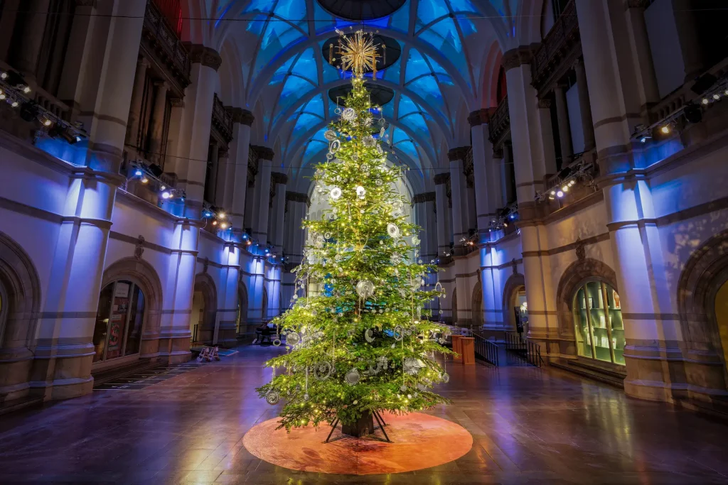En hög julgran i en stor hall med stjärnor, solar, och gnistrande kristaller