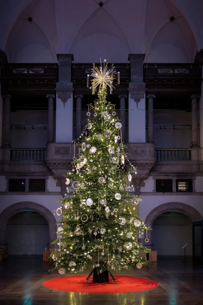 En hög julgran i en stor pampig hall klädd med gnistrande stjärntecken, solar och stjärnfall gjorda av gamla kakformar