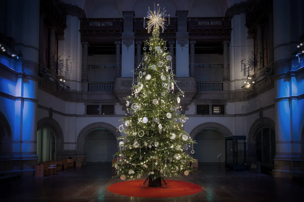 En hög julgran i en stor pampig hall klädd med gnistrande stjärntecken, solar och stjärnfall gjorda av gamla kakformar