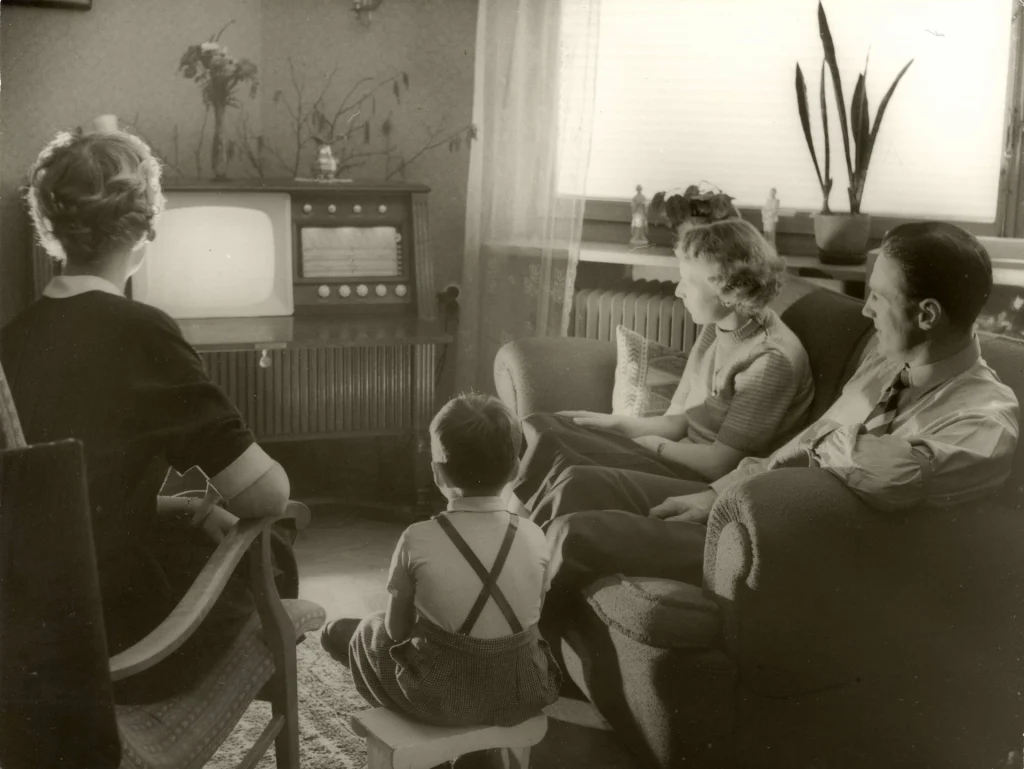 Barn och vuxna tittar på TV på en kombinerad TV- och radiomöbel i vardagsrum.