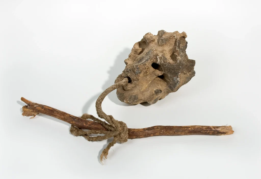 Närbild på en skrovlig sten med borrade hål i, fäst i en gren med ett snöre