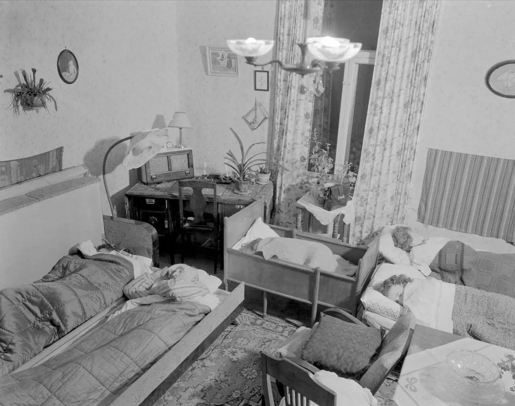 Ett vardagsrum med en sovande familj på utvikssängar, två vuxna och tre barn