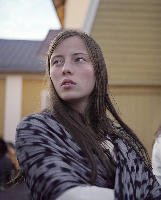 En ung tjej med långt hår och sjal runt axlarna blickar ut ur bild