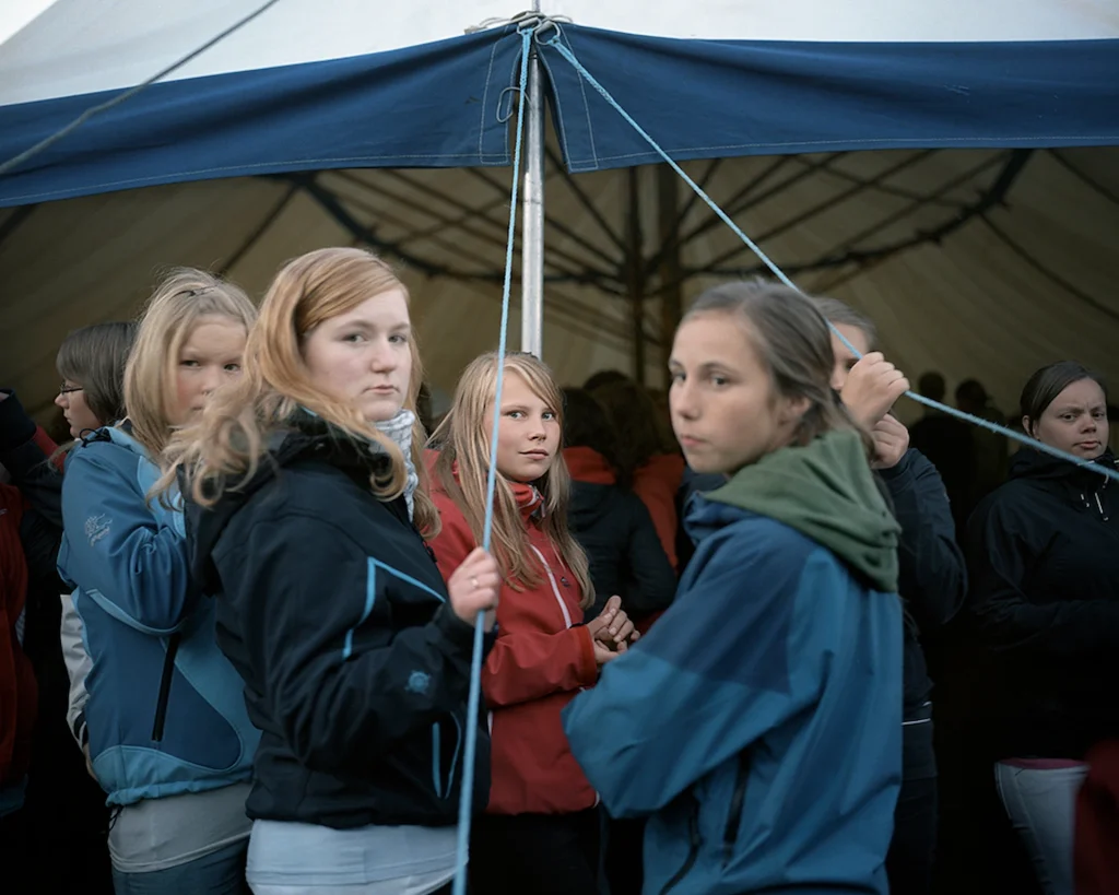 en grupp unga tjejer står i grupp utanför ett tältmöte, de är klädda i friluftsjackor som om det är en kylig vårkväll