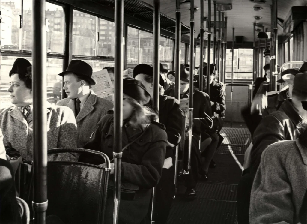 Passagerare sitter tätt i en buss och läser eller tittar ut genom fönstren under en resa i stadsmiljö.