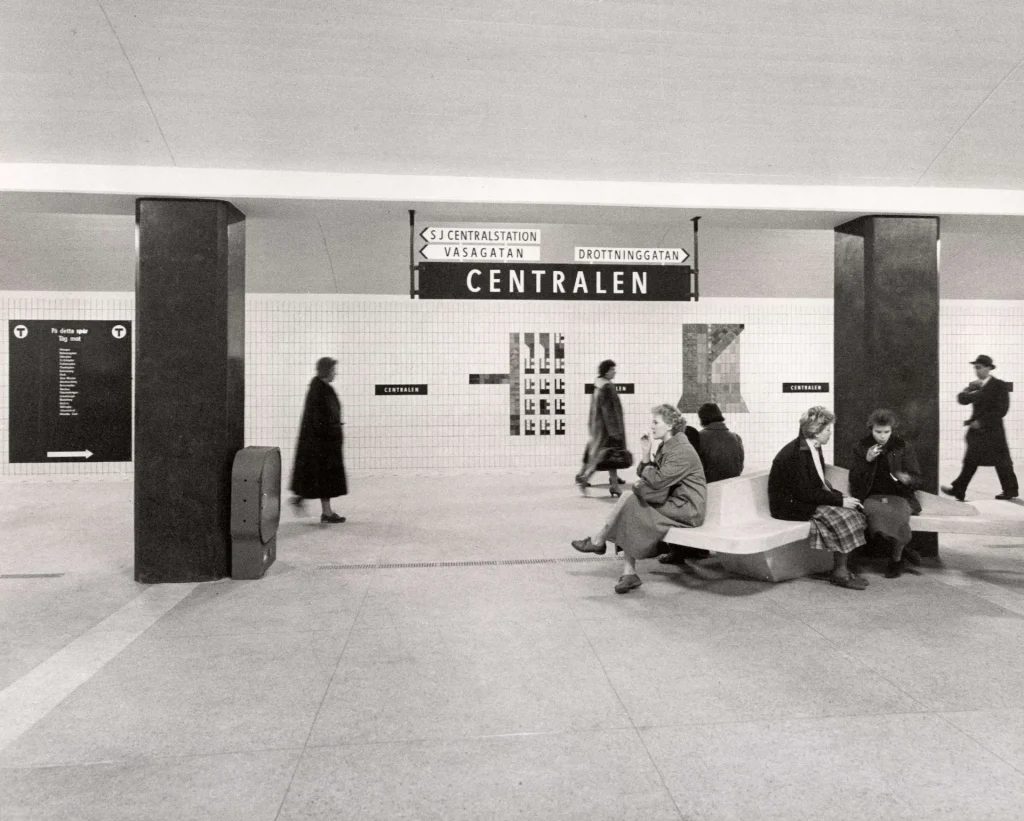 Resenärer väntar och sitter på bänkar vid stationen Centralen, medan andra passerar förbi i rörelse.