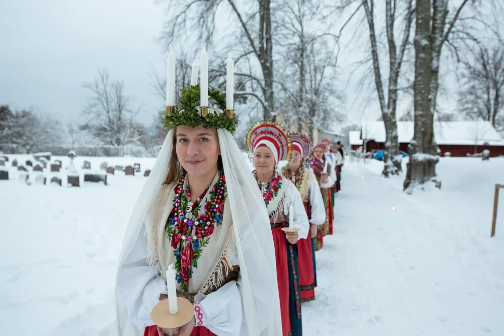 Ett luciatåg i folkdräkter är fotograferade utomhus i snön.